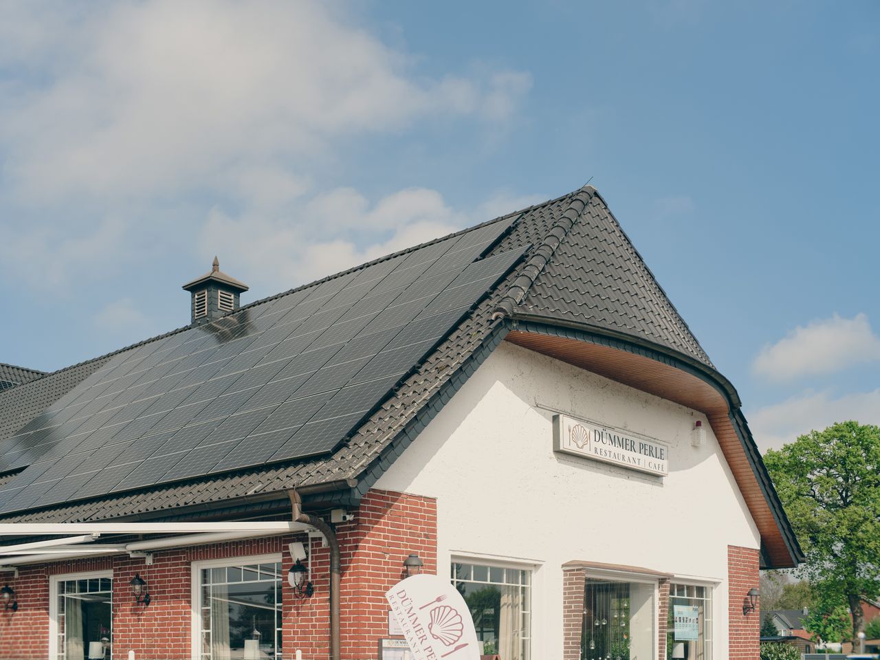 services-03 A red brick building with solar panels on the roof, under a clear blue sky, symbolizing sustainability and renewable energy.