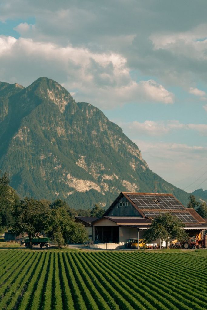 scenic-swiss-farm-with-solar-powered-barn-33900746 Captivating view of a solar-powered barn amidst lush Swiss fields and alpine mountains.